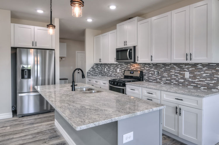 Recently renovated kitchen with gleaming granite pantries, in shades of gray, and white cabinets.
